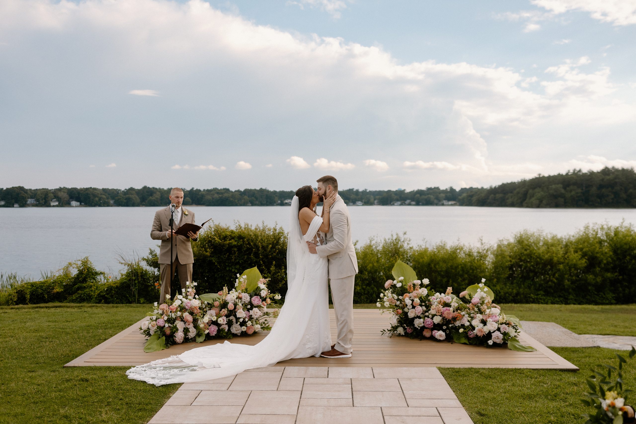 Bride and groom kiss during their late June wedding ceremony at The Lakehouse in Halifax, MA — a fully edited lakeside wedding photo